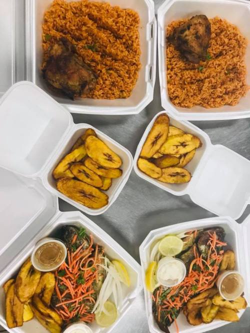 A spread of takeout containers featuring jollof rice, grilled chicken, fried plantains, and fresh vegetables.