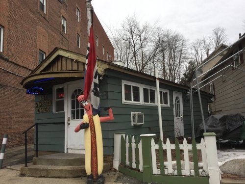 A quirky diner with a hot dog mascot outside, featuring a flag and a cozy, inviting entrance.