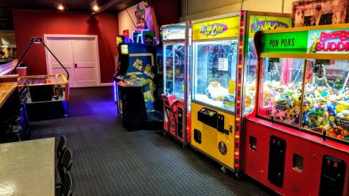 A colorful arcade with claw machines, air hockey, and video game cabinets in a dimly lit room.