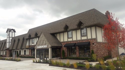A charming building with a steep roof, featuring a sign that reads "Sanders" and surrounded by landscaping and trees.