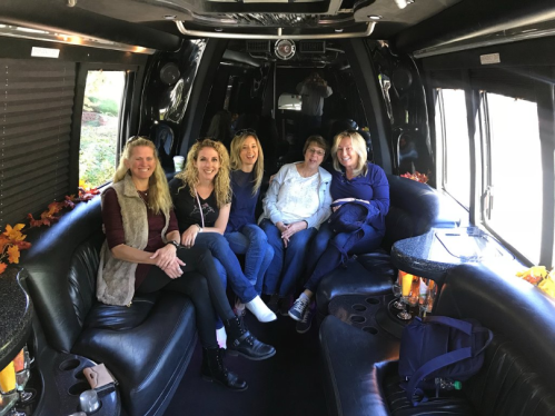 A group of five women sitting together inside a stylish black limousine, smiling and enjoying their time.