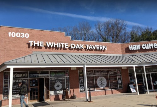 Exterior of The White Oak Tavern, featuring a brick facade and signage, with trees in the background.