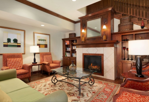 Cozy living room with a fireplace, comfortable seating, a glass coffee table, and decorative artwork on the walls.