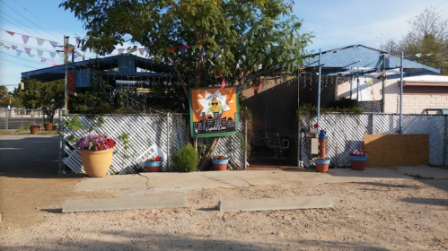 A colorful outdoor restaurant entrance with potted plants and festive decorations under a clear blue sky.