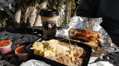 A takeout meal with enchiladas, rice, and beans, accompanied by a coffee cup and two containers of sauce.