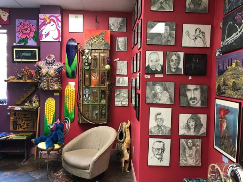 A colorful art gallery wall featuring various framed drawings, sculptures, and decorative items in a vibrant setting.
