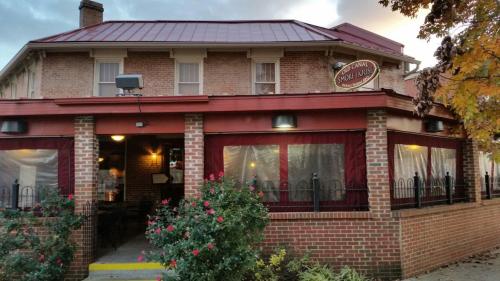 A brick restaurant with a red roof and outdoor seating, surrounded by flowers and trees, under a cloudy sky.