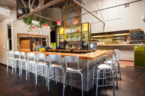 A modern bar with a wooden counter, metal stools, and shelves filled with various bottles in a stylish interior.