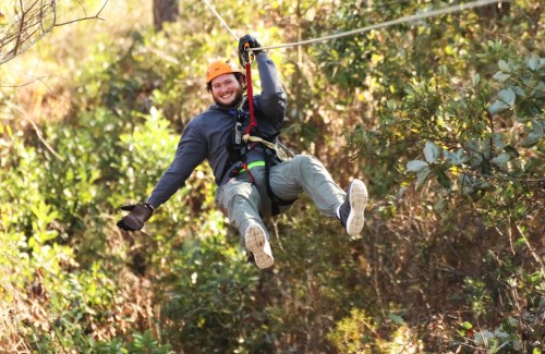 A person in a helmet zip-lining through a forest, smiling and enjoying the adventure.