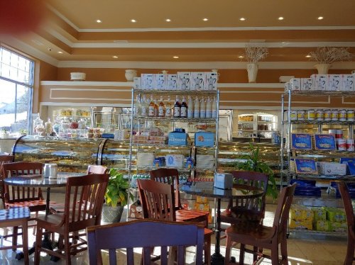 A bright café interior with glass display cases filled with pastries and shelves stocked with various products.