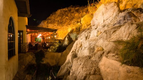 A cozy outdoor restaurant illuminated at night, nestled against rocky terrain and surrounded by warm lighting.