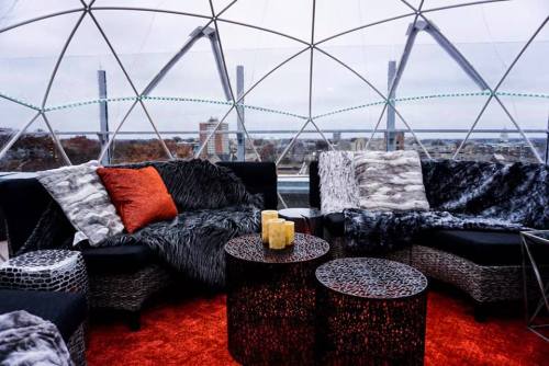 Cozy indoor seating in a geodesic dome, featuring plush cushions, candles, and a vibrant orange rug.