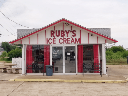 A small ice cream shop with a red and white exterior, featuring "Ruby's Ice Cream" sign and outdoor seating.