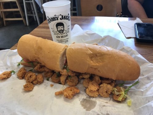 A long sandwich filled with shrimp and lettuce, resting on a table next to a cup from a restaurant.
