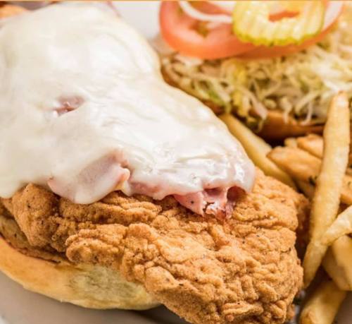 A crispy fried chicken sandwich topped with melted cheese, served with lettuce, tomato, pickles, and fries on the side.