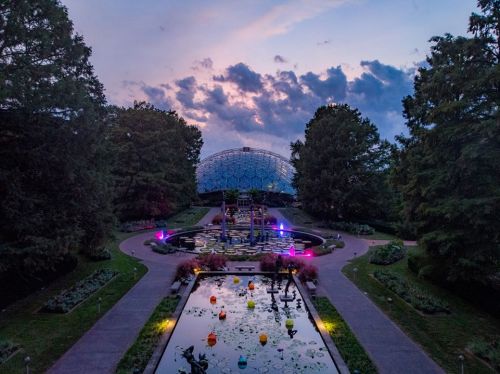 A serene garden at dusk, featuring a pond with colorful floats and a geodesic dome in the background.