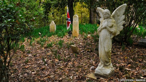 A serene graveyard scene featuring a stone angel statue and a Confederate flag among tombstones and greenery.