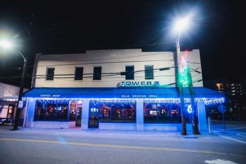 A brightly lit restaurant exterior at night, featuring "Tower 7" signage and festive lights.
