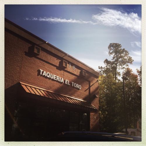Sign for "Taqueria El Toro" on a brick building under a clear blue sky. Trees are visible in the background.