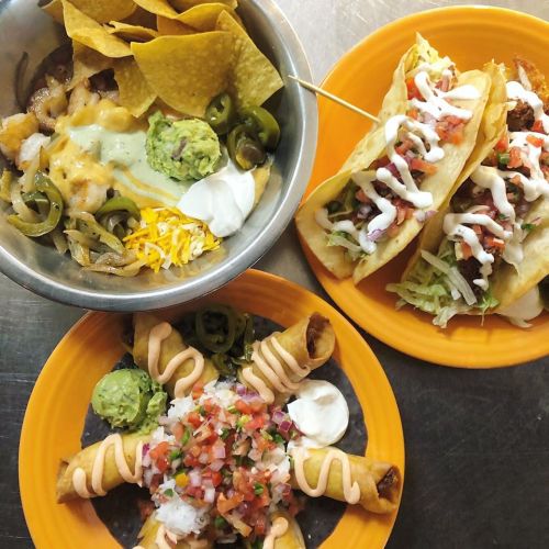 A colorful spread of tacos, nachos, and taquitos with toppings like guacamole, sour cream, and pico de gallo.