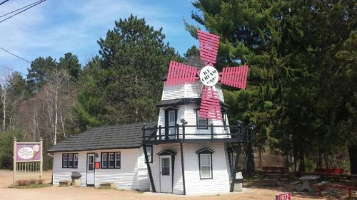 A small, white building with a red windmill on top, surrounded by trees and a sign nearby.