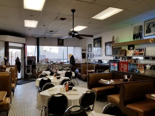 A cozy diner interior with booths, a counter, and vintage decor, featuring checkered floors and large windows.