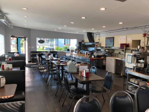 A bright, modern diner interior with black booths, tables, and an open kitchen area.