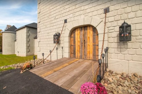 A rustic wooden door with metal accents, flanked by lanterns, set against a stone wall and surrounded by flowers.
