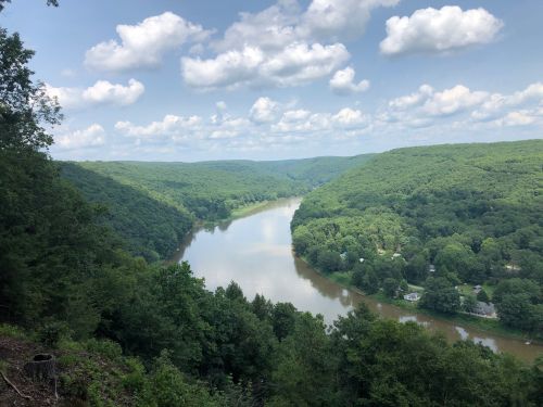 A scenic view of a winding river surrounded by lush green hills and a blue sky with fluffy clouds.