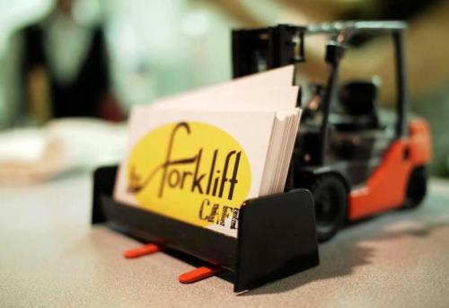 A small forklift model holding business cards with a yellow logo that reads "the forklift cam."