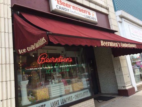 A storefront with a red awning reading "Beernsten's Confectionary" and neon signs for candy and ice cream.