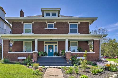 A large brick house with a blue front door, surrounded by a well-maintained garden and clear blue sky.