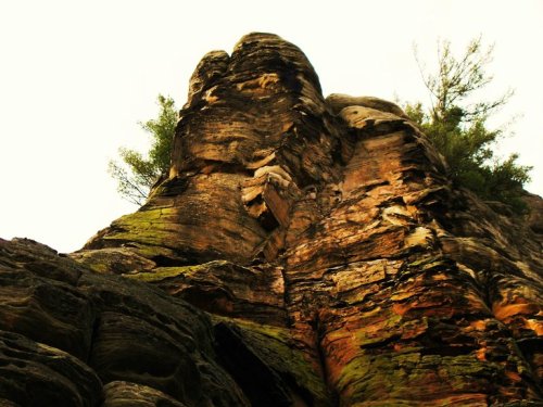 A towering rock formation with moss and trees, set against a cloudy sky.