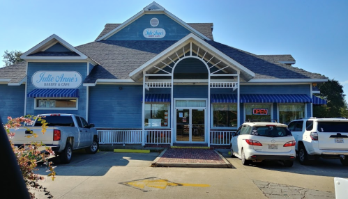 A blue bakery and café with a sign reading "Julie Anne's Bakery & Café" and several parked cars outside.