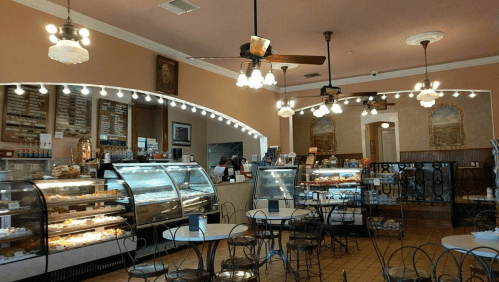Cozy café interior with display cases of pastries, round tables, and vintage decor under warm lighting.