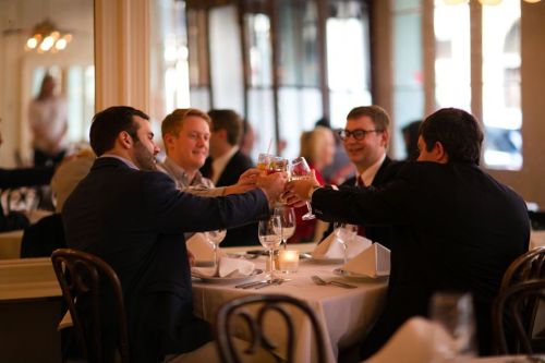 A group of four men toasting with drinks at a restaurant table, enjoying a celebratory moment together.