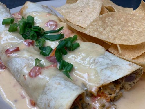 A plate of enchiladas topped with creamy sauce, diced tomatoes, and green onions, served with tortilla chips.