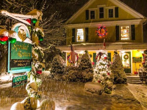 A cozy yellow house decorated for Christmas, surrounded by snow, with festive wreaths and a sign reading "Spoiled Rotten."