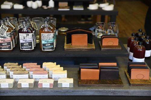 A display of various handmade soaps, leather wallets, and beverages on wooden shelves in a shop.