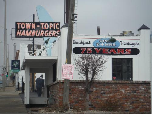 Sign for Town-Topic Hamburgers, featuring "75 Years" and "Open 24 Hrs," with a person walking by in the foreground.