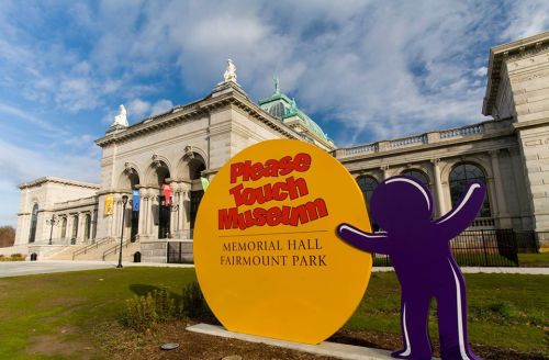 Sign for the Please Touch Museum in Fairmount Park, with Memorial Hall in the background and a blue sky above.