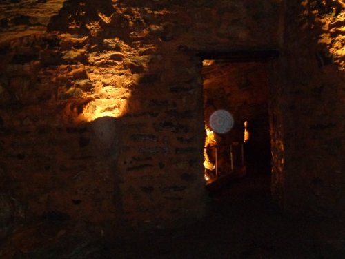 Dimly lit stone cave entrance with warm lighting illuminating the walls and a circular object in the foreground.