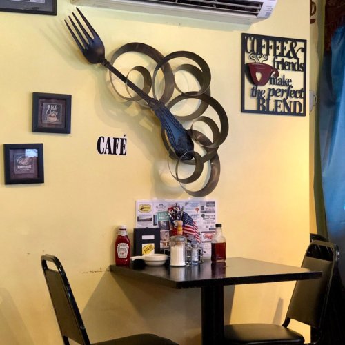 A cozy café interior with a decorative fork on the wall, a table set with condiments, and a menu on the table.