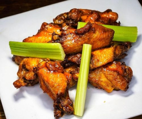 A plate of crispy chicken wings garnished with celery sticks.