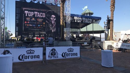 A stage setup for the Top Taco event, featuring a large screen and palm trees in the background.