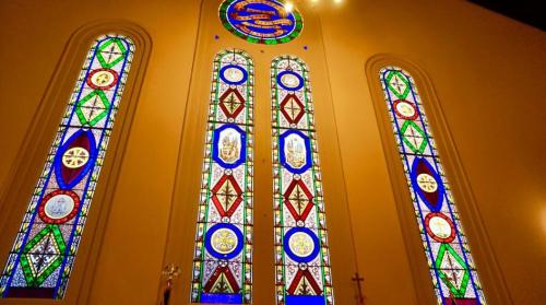 Colorful stained glass windows featuring intricate designs and symbols, illuminating the interior of a church.