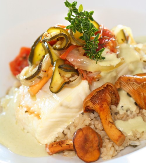 A plate of fish topped with sautéed vegetables and herbs, served over a bed of rice with mushrooms on the side.