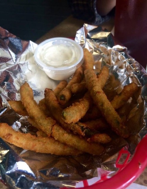 A basket of crispy fried green beans with a small cup of dipping sauce on the side, wrapped in foil.