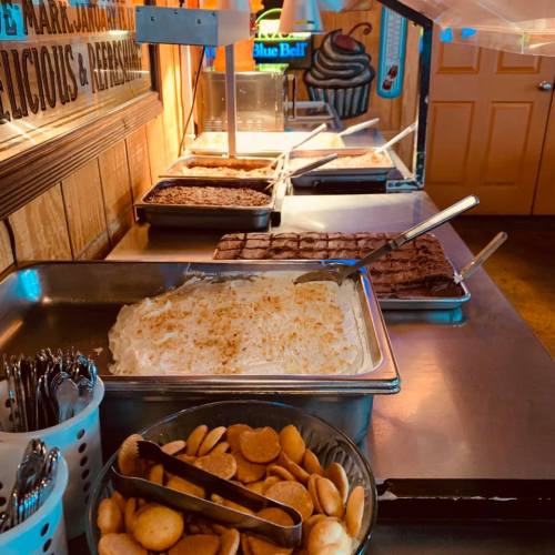 Dessert buffet featuring various treats, including cakes, brownies, and whipped cream, with utensils and serving trays.