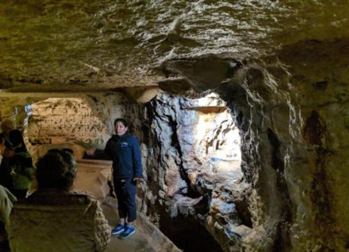 A tour guide stands in a dimly lit cave, explaining the surroundings to a small group of visitors.